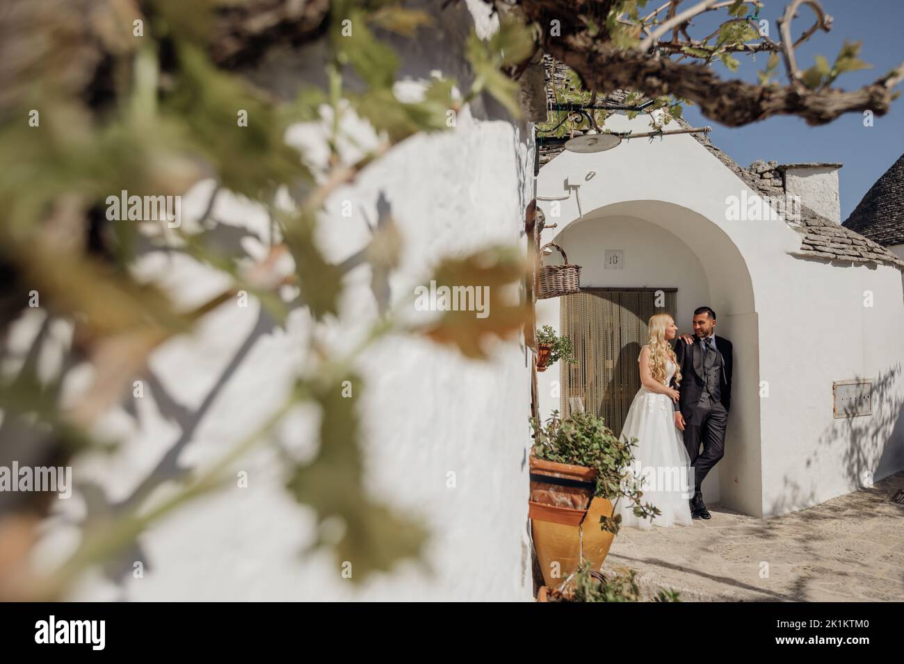 Portrait eines Ehepaares, das unter dem Bogen eines alten weißen Steinhauses mit kegelförmigem Dach steht und spricht. Hochzeit. Stockfoto