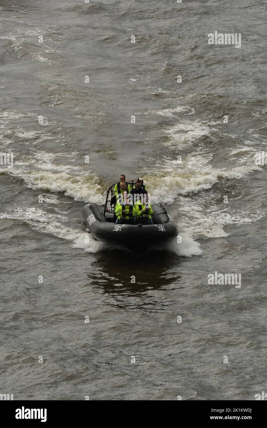 Die vertikale Ansicht von Menschen mit grünen Schwimmwesten im RIB Schnellboot auf den Wellen Stockfoto