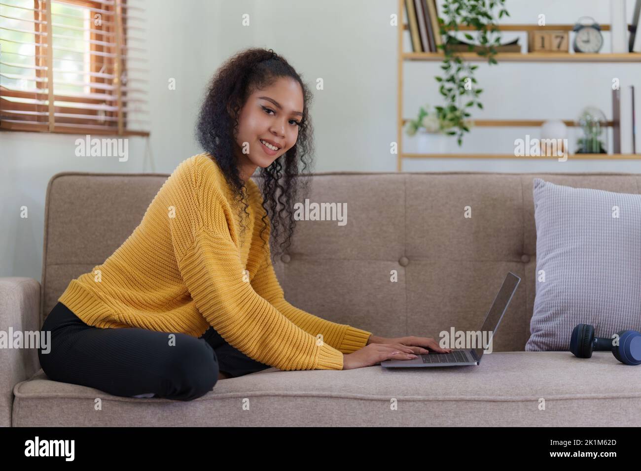 Attraktive lächelnde junge Frau mit Laptop auf Sofa zu Hause. Lifestyle-Konzept Stockfoto