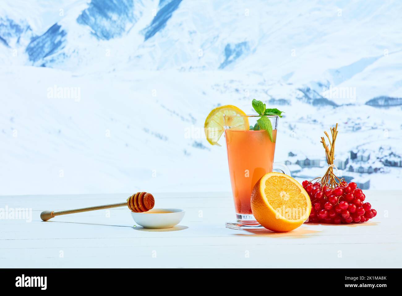 Glas mit Orangentee oder Cocktail, Beeren und Honig auf weißem Tisch vor dem Hintergrund der winterlich schneebedeckten Berge. Gesundheit, Pflege, Liebe Stockfoto
