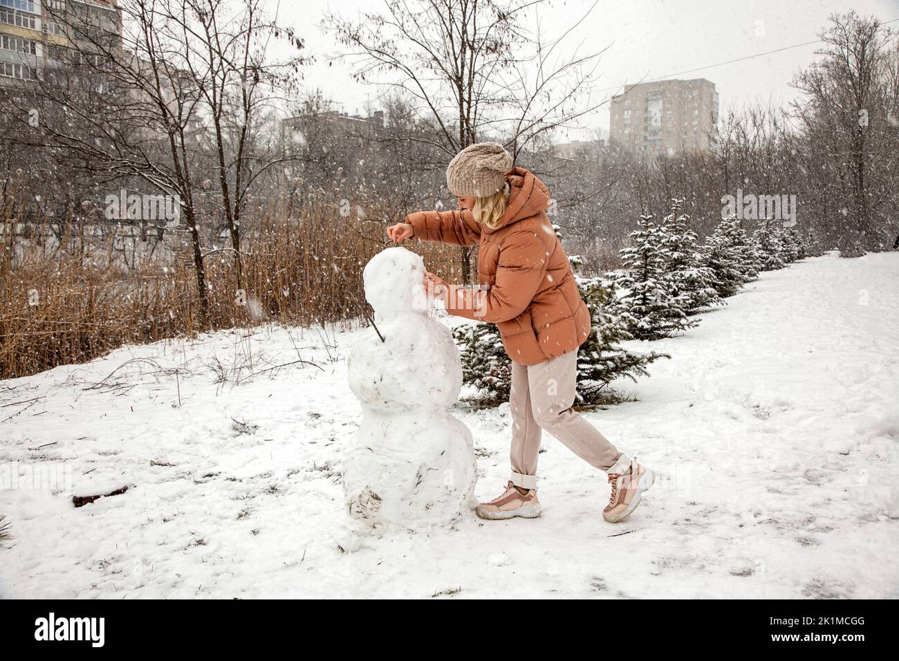 Frau macht einen Schneemann in einem Stadtpark während eines Schneefalls. Stockfoto