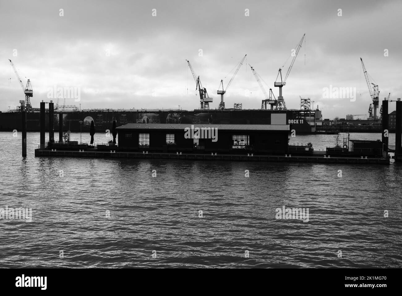Die Graustufen eines schwimmenden Cafés auf dem Wasser vor den Kränen im Hamburger Hafen Stockfoto