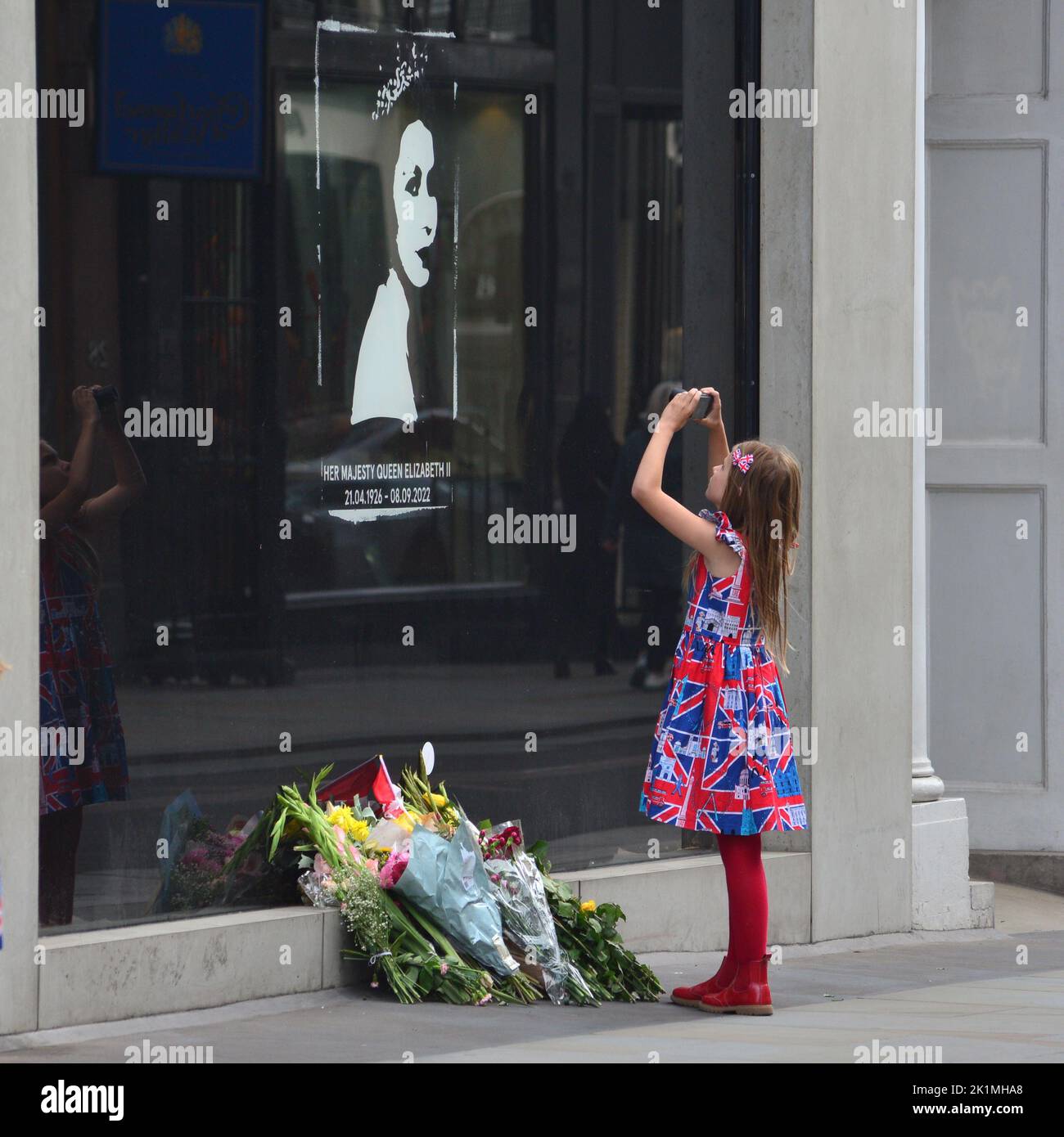 Staatsbegräbnis Ihrer Majestät Königin Elizabeth II., London, Großbritannien, Montag, 19.. September 2022. Ein junges Mädchen in einem Kleid von Union Jack, das in einem Schaufenster in der Old Bond Street ein Erinnerungsfoto von Ihrer Majestät der Königin fotografiert. Stockfoto