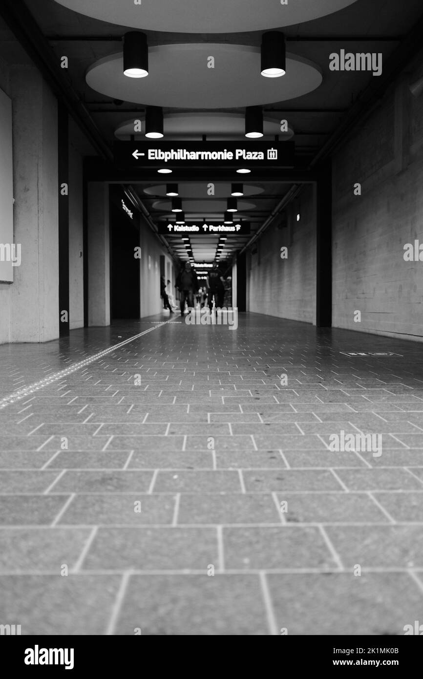 Die senkrechte Graustufe eines langen Korridors und ein Schild, das zur Elbphilharmonie plaza führt Stockfoto