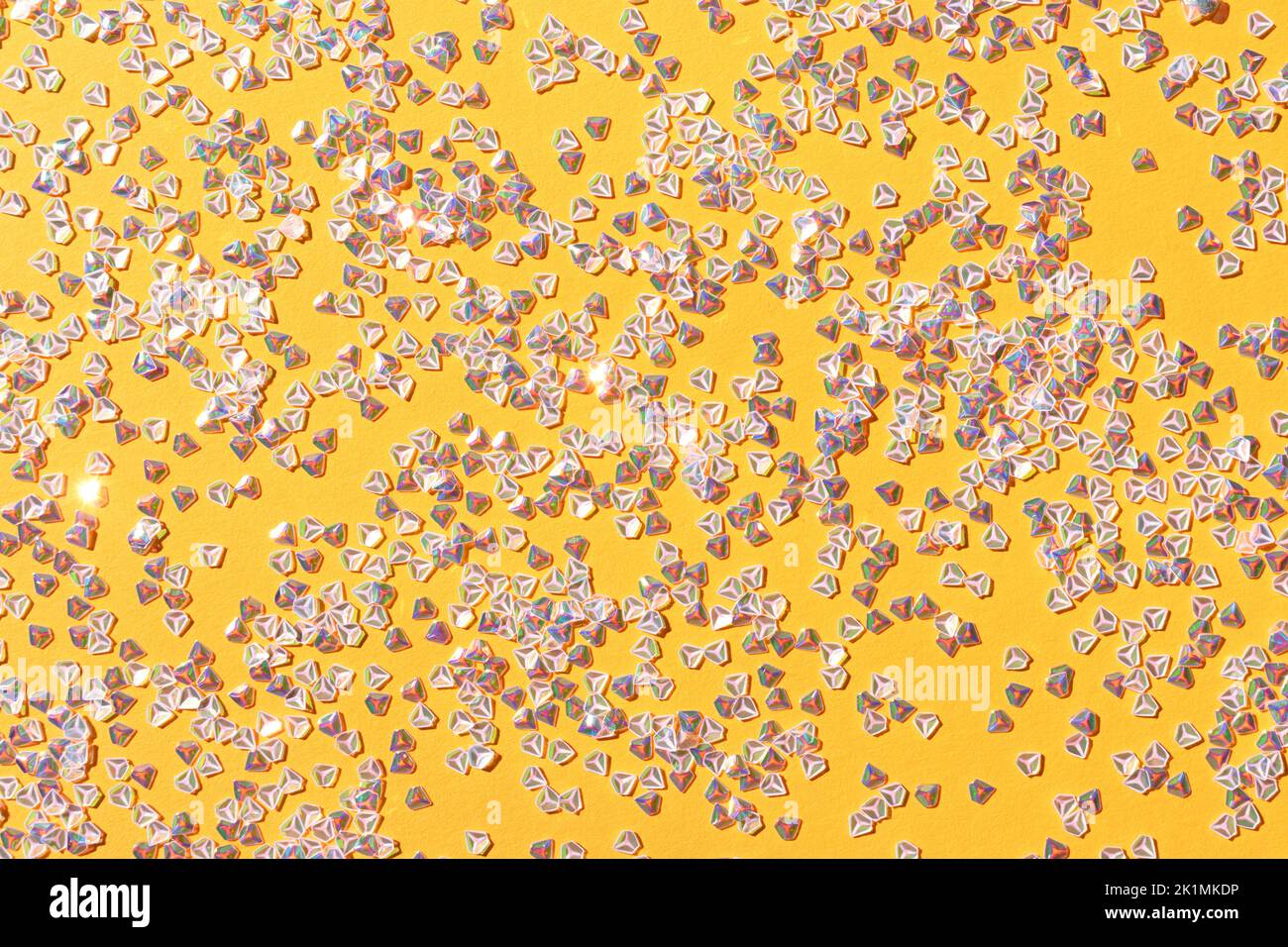 Winziges Konfetti aus silbernem Kristall auf gelbem Hintergrund. Leuchtende festliche Textur. Stockfoto