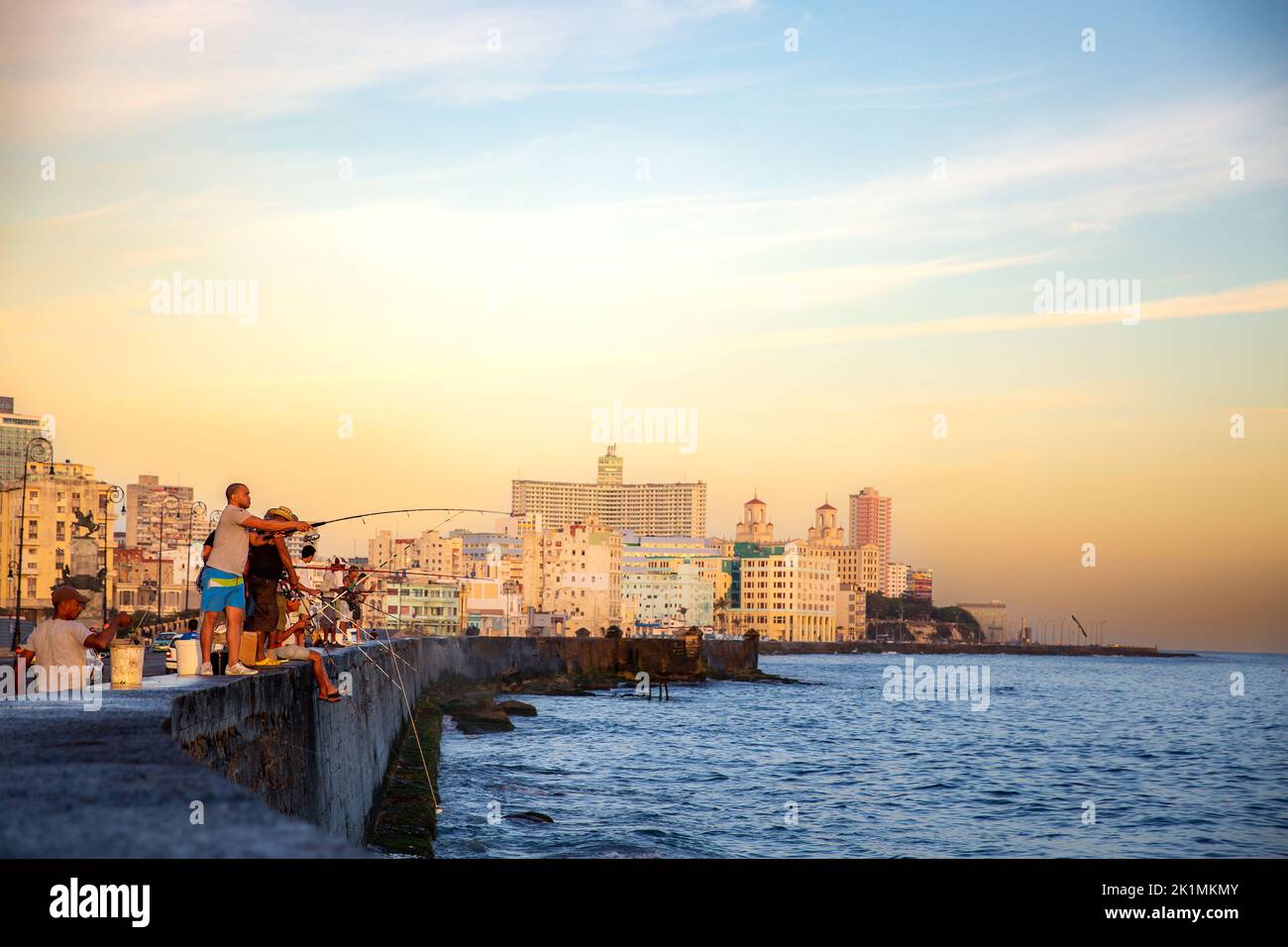 Eine Aufnahme von Menschen, die aus dem Meer mit Gebäuden im Hintergrund in Kuba fischen Stockfoto