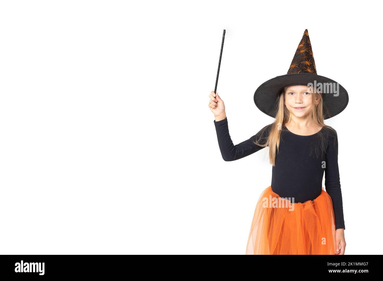 Halloween Für Kinder. Ein schönes niedliches Mädchen in einem Hexenkostüm, trägt einen Hut und mit einem Zauberstab zeigt einen leeren Raum auf einem weißen Hintergrund Studio, Kopie Stockfoto