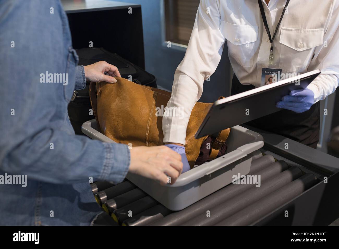 Sicherheitsagent am Flughafen hilft der Frau bei der Inspektion, den Laptop zu entfernen Stockfoto