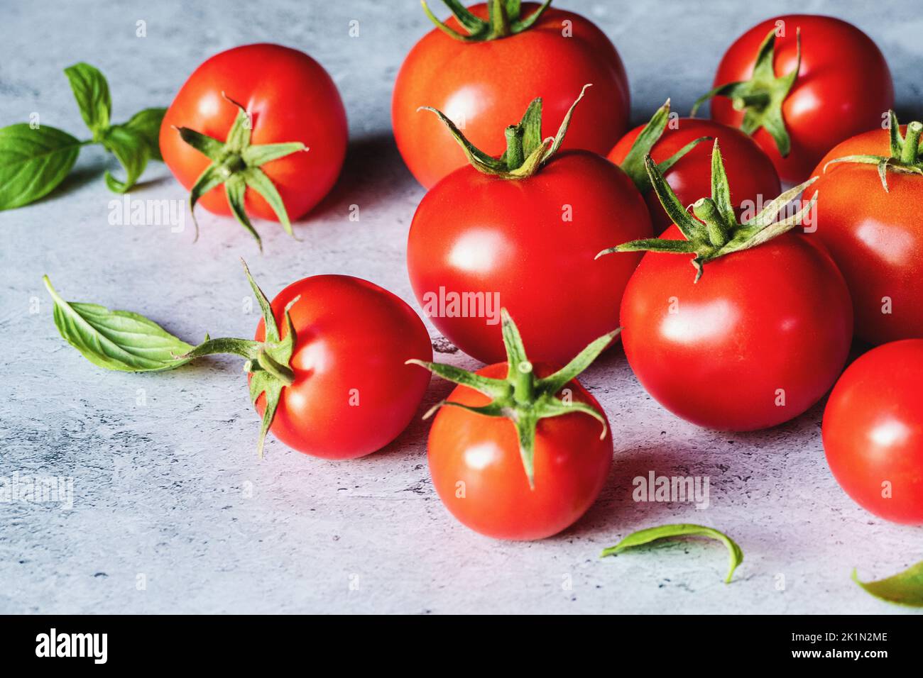 Rote Tomaten mit grünen Basilikumblättern auf grauem Betongrund, selektiver Fokus Stockfoto