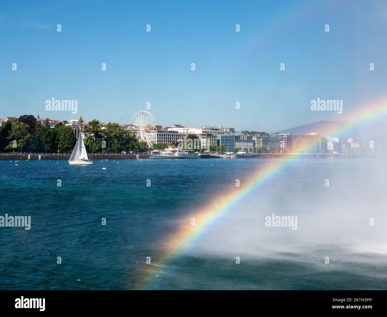 Genf, Schweiz - 13. Juli 2022: Regenbogen aus dem Wasserstrahl über dem Genfer See und Blick auf die Stadt Genf Stockfoto