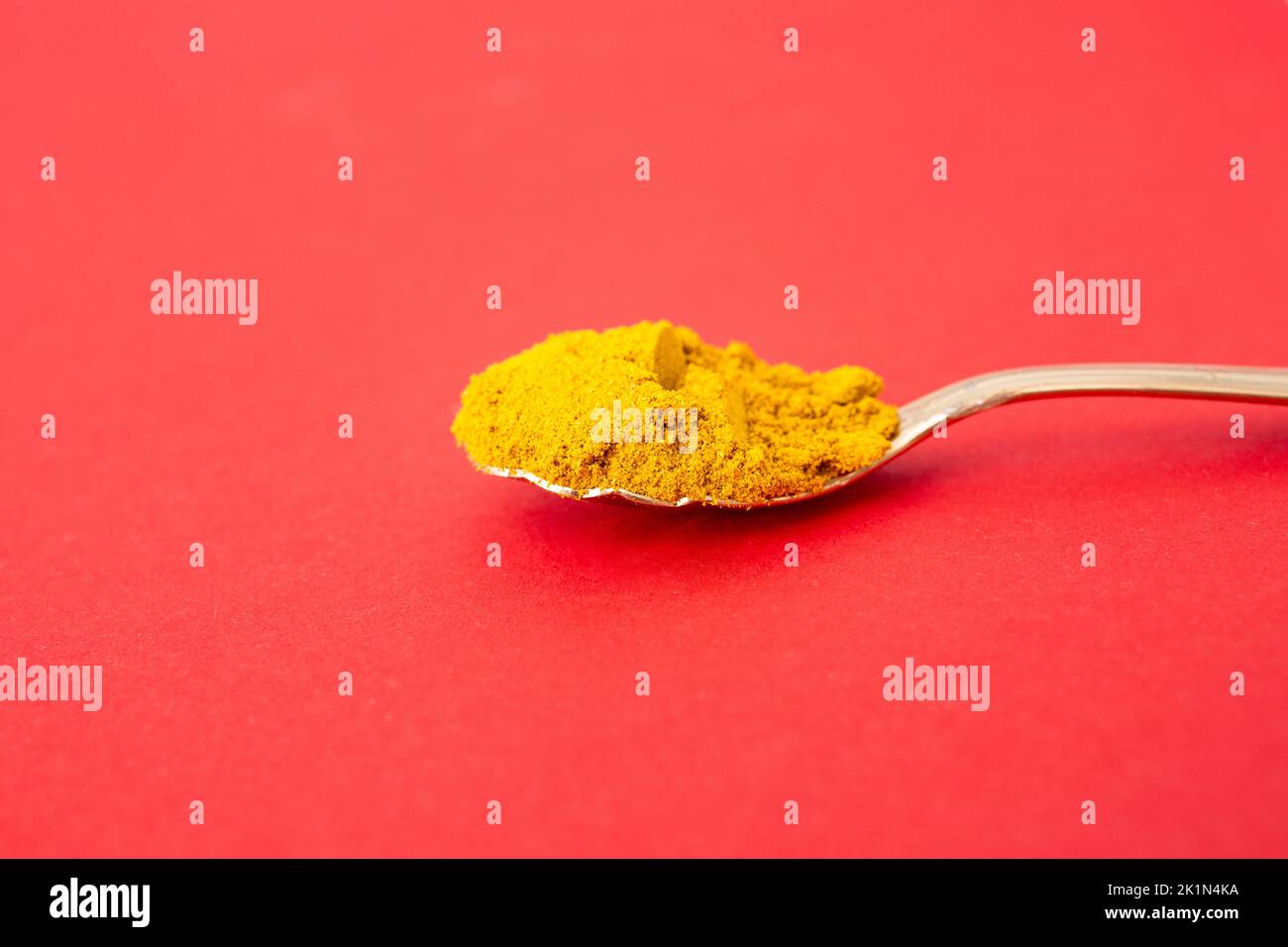 Golden Tea Löffel voll Curry Pulver, isoliert auf rotem Hintergrund, Seitenansicht weichen Fokus Nahaufnahme. Stockfoto