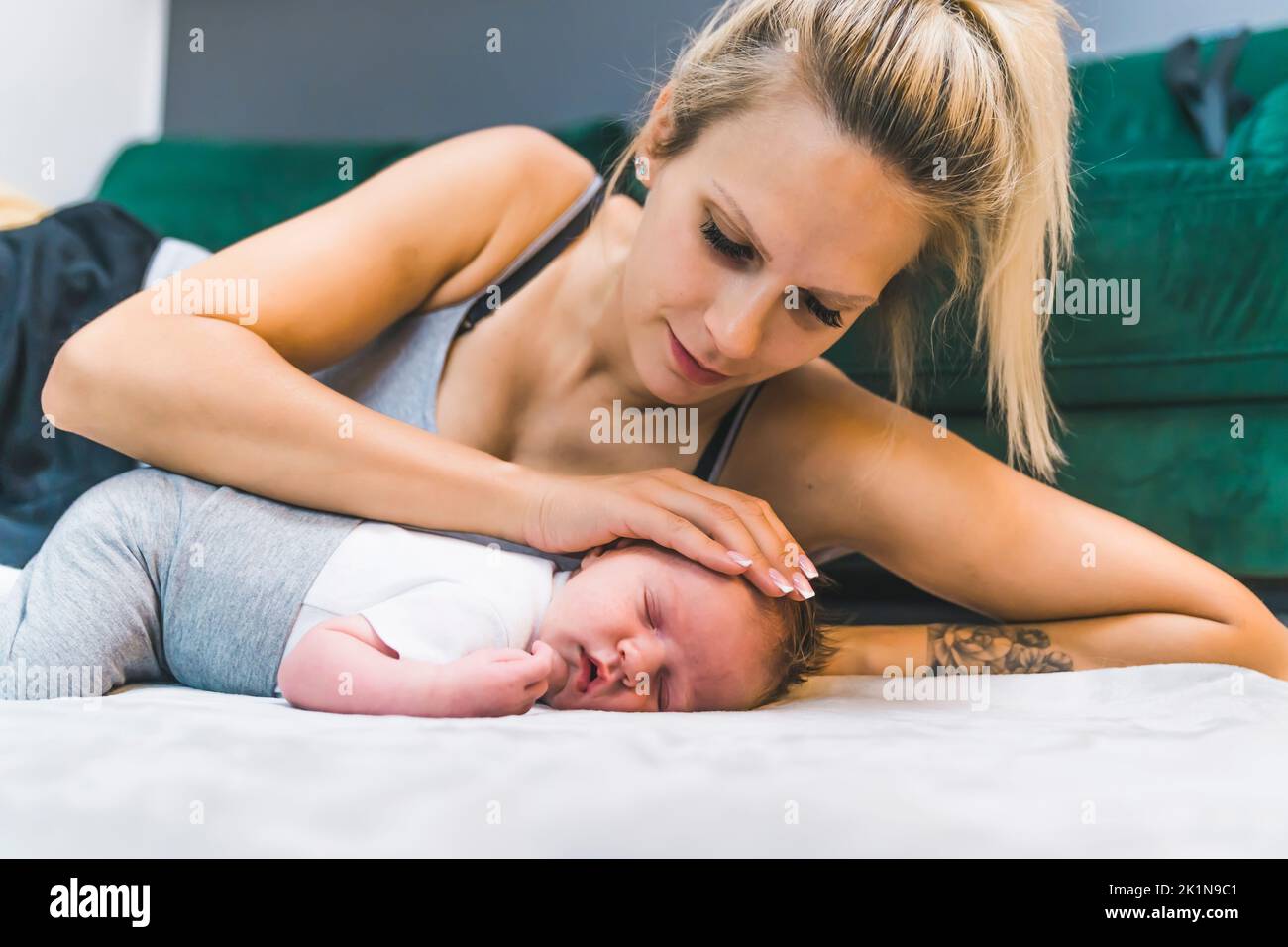 Blonde weiße Frau, die auf der Seite auf dem Boden liegt und den Kopf ihres kleinen Jungen streichelt, der sich neben ihr auf einer Decke ausruht. Fürsorgliche, zärtliche Mutter. Horizontale Innenaufnahme. Hochwertige Fotos Stockfoto
