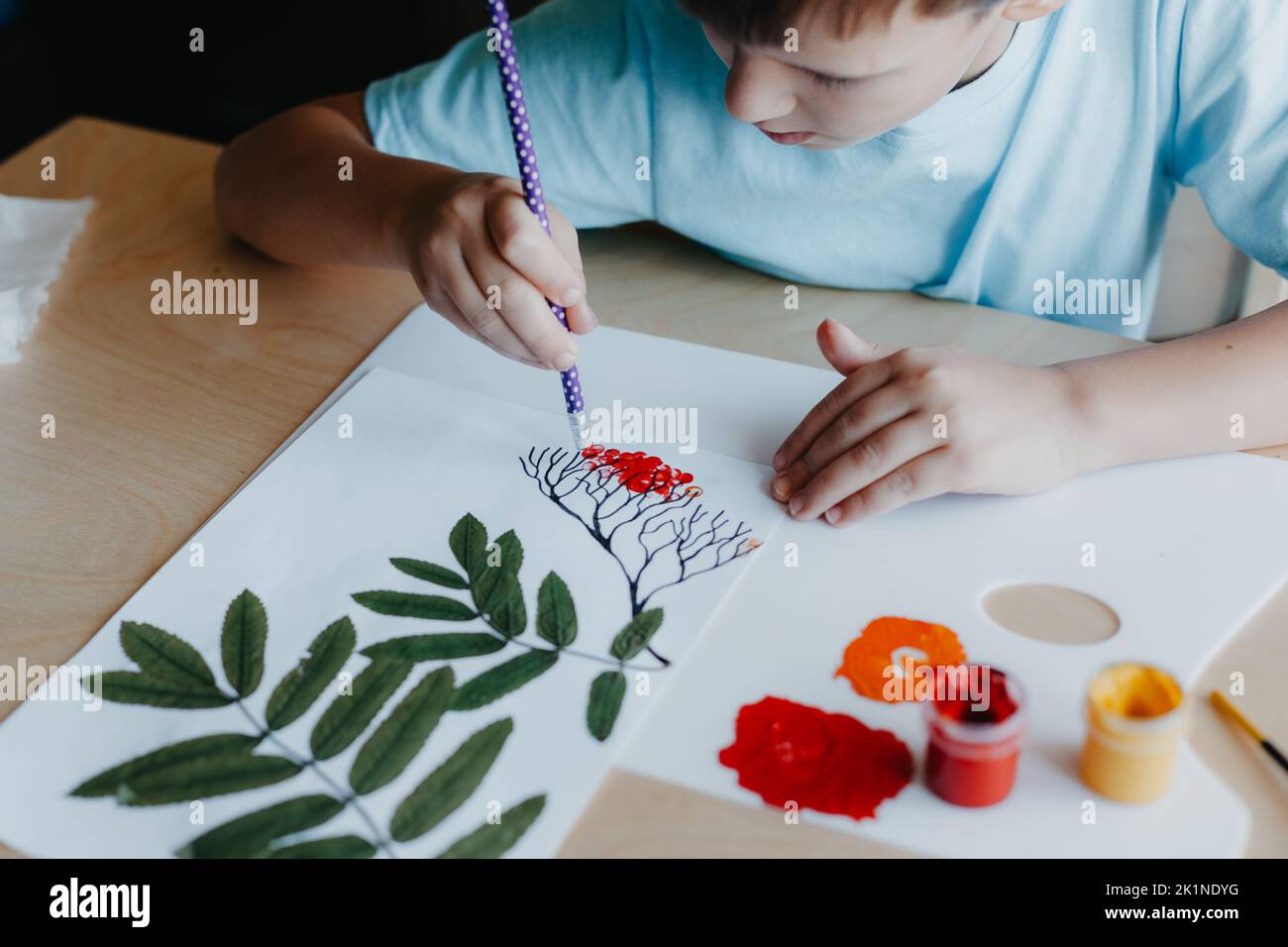 Niedliches Kind sitzt am Schreibtisch und zeichnet Vogelbeeren auf