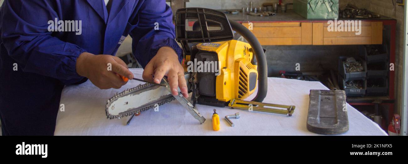 Bild eines Handwerkers, der die Kette einer Kettensäge mit einer Feile schärft. Vorbereitung von Werkzeugen für das Schneiden von Holz in Erwartung des Winters. Do-it-yourself Stockfoto