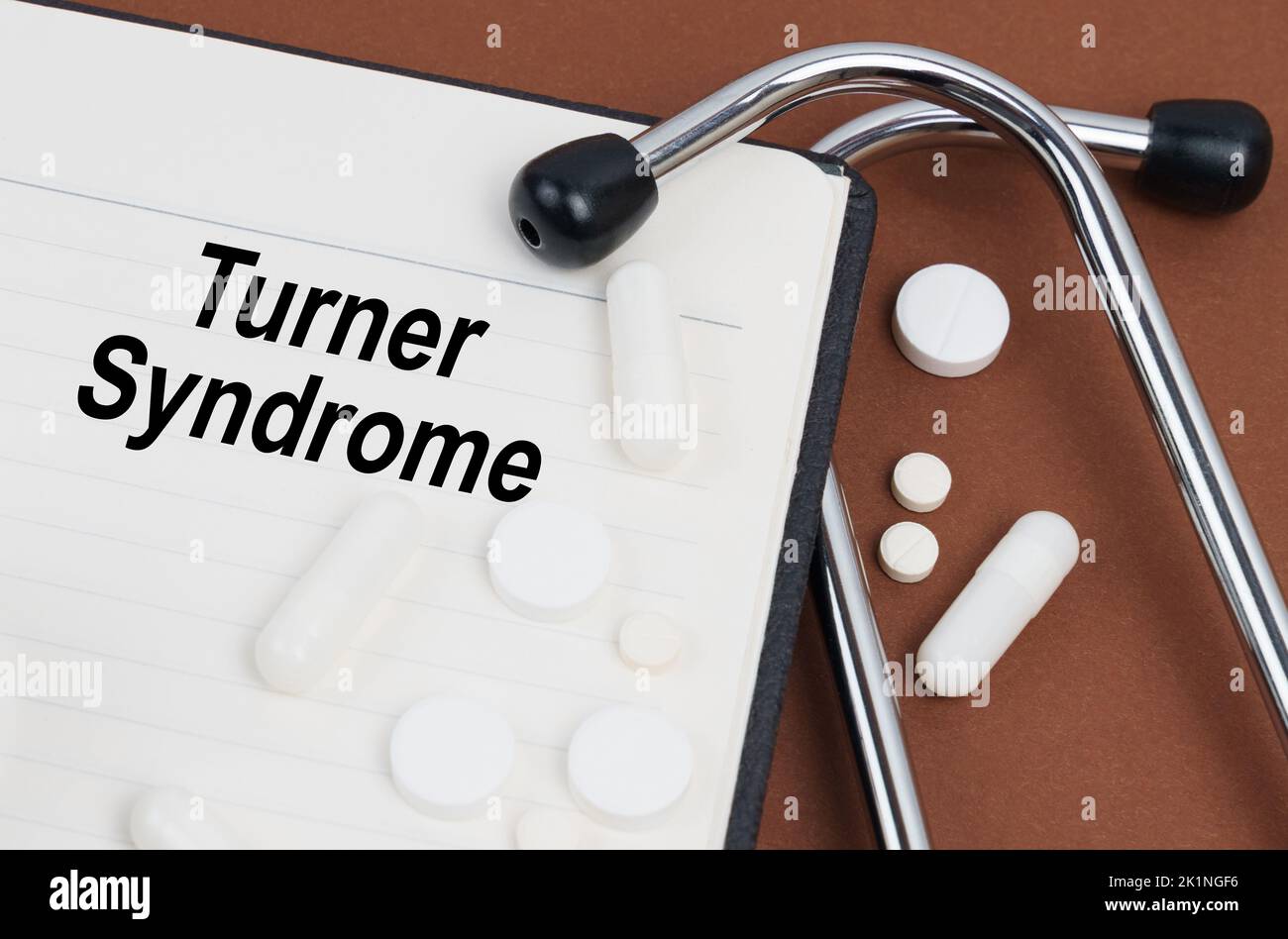 Medizinisches Konzept. Auf einer braunen Oberfläche liegt ein Stethoskop, Pillen und ein Notizblock mit der Aufschrift - Turner Syndrome Stockfoto