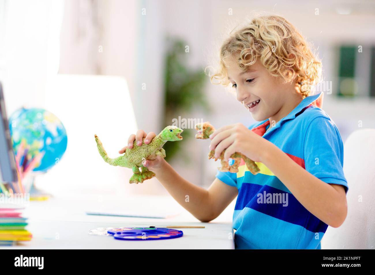 Online-Fernunterricht. Schulkinder mit Computer, die mit dem Lehrer und der Klassengruppe über Videokonferenzen chatten. Kind Färbung Ton Dinosaurier. Stockfoto