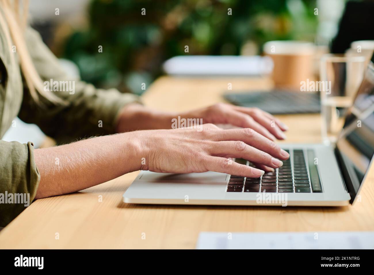 Seitenansicht der Hände einer jungen Geschäftsfrau, die auf der Laptop-Tastatur tippt, während sie im Büro oder Café am Tisch sitzt und an einem Projekt arbeitet Stockfoto