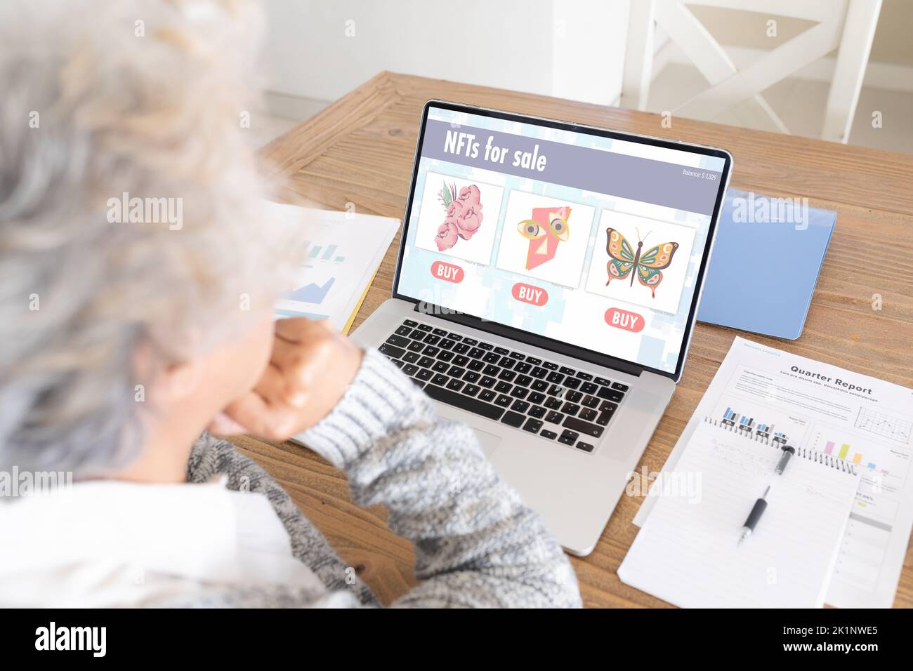 Kaukasische ältere Frau, die zu Hause nicht-fungible Token über einen Laptop kauft Stockfoto