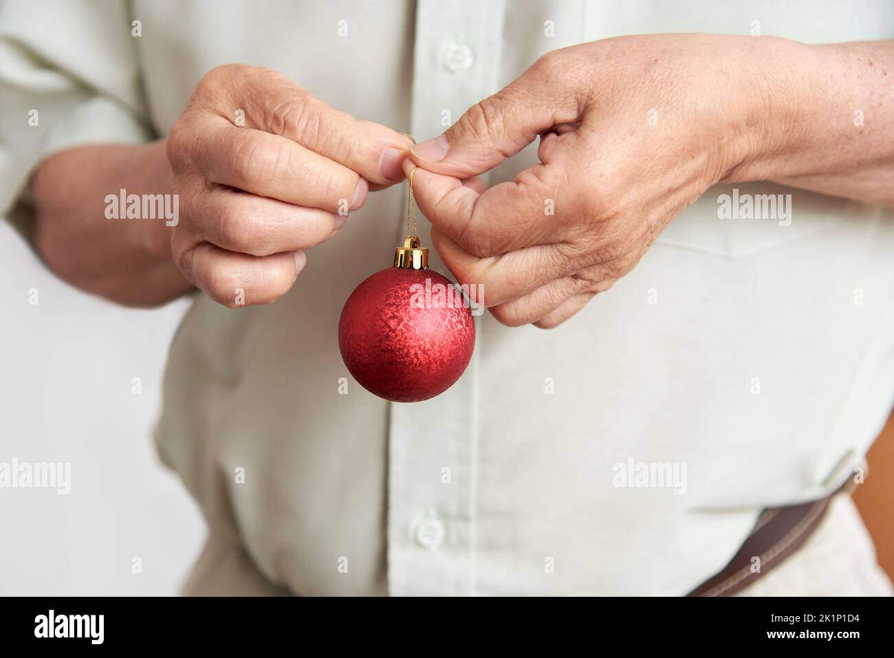 Nicht erkennbarer älterer Mann, der zu Hause einen Weihnachtsbaum schmückt, männliche Hände, die eine rote strukturierte Kugel halten. Stockfoto