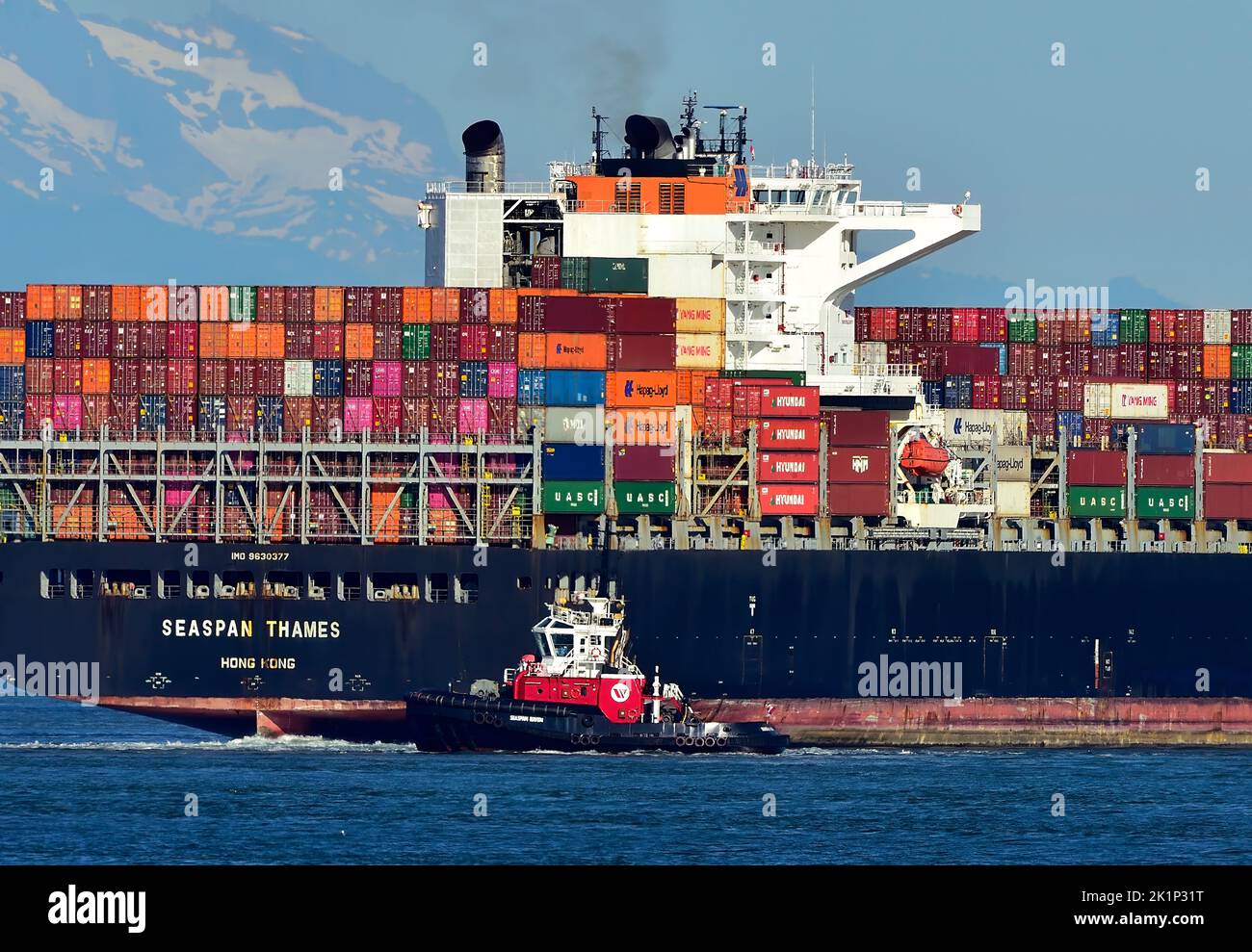 Ein mit Containern beladenes Seeschiff, das mit einem Schlepper in den Hafen von Vancouver gelenkt wird. Stockfoto