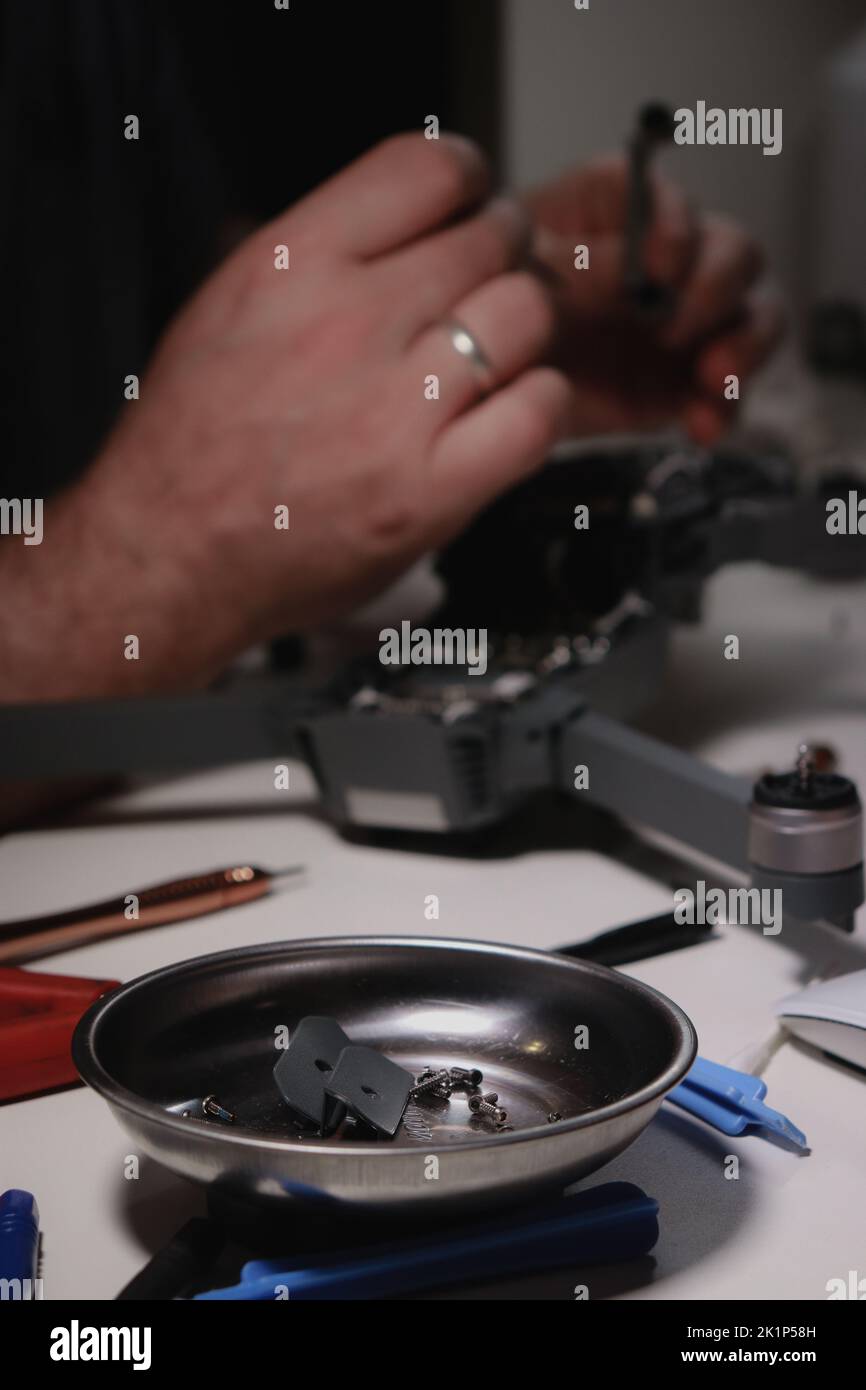 Nahaufnahme der Hände von mans, die eine Drohne auf einem weißen Tisch mit verschiedenen Werkzeugen reparieren Stockfoto