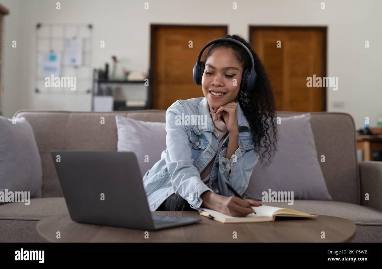 Mixed Race Frau trägt Kopfhörer beobachten Webinar schreiben Notizen Studie online mit Online-Lehrerin, afrikanischer Studentin lernen Sprache Computer Stockfoto