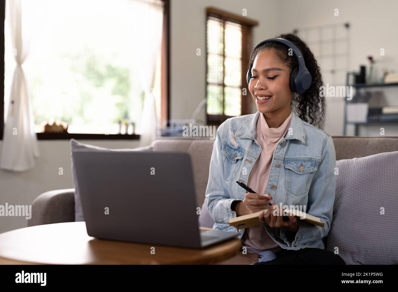 Mixed Race Frau trägt Kopfhörer beobachten Webinar schreiben Notizen Studie online mit Online-Lehrerin, afrikanischer Studentin lernen Sprache Computer Stockfoto