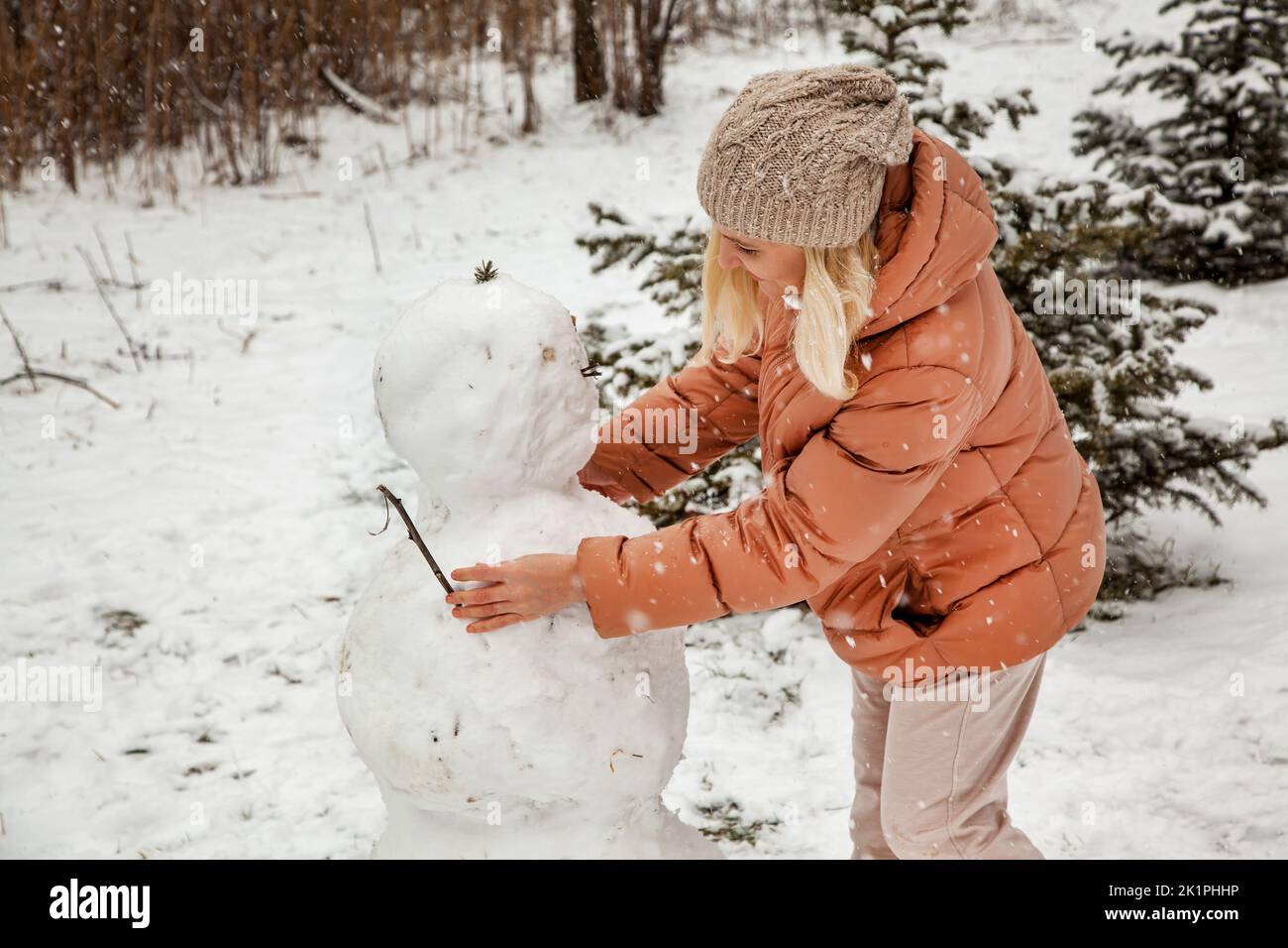 Frau macht einen Schneemann in einem Stadtpark während eines Schneefalls. Stockfoto