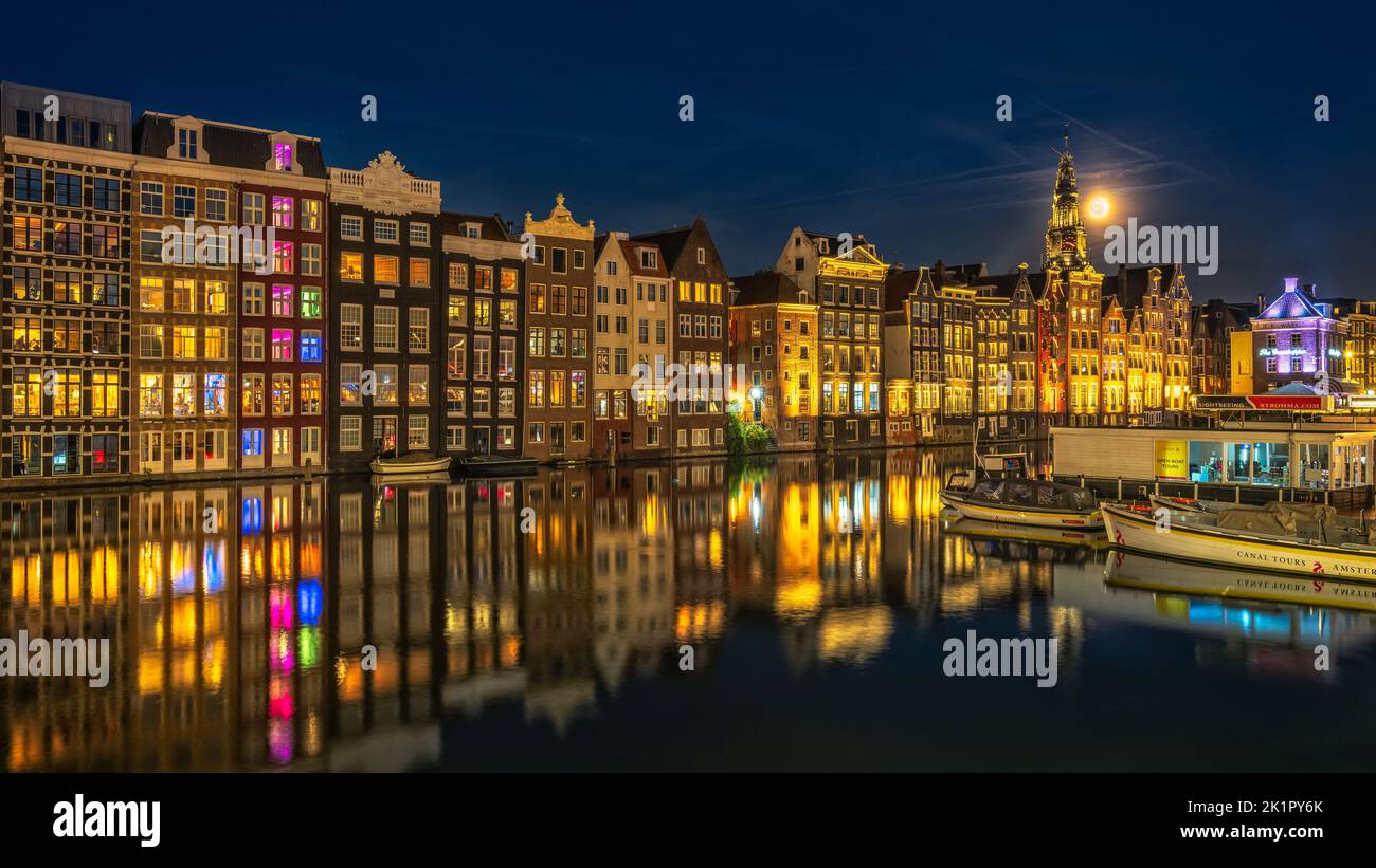 damrak Häuser am Wasser mit ihren Spiegelungen im Wasser in amsterdam während der Bluesthour Stockfoto