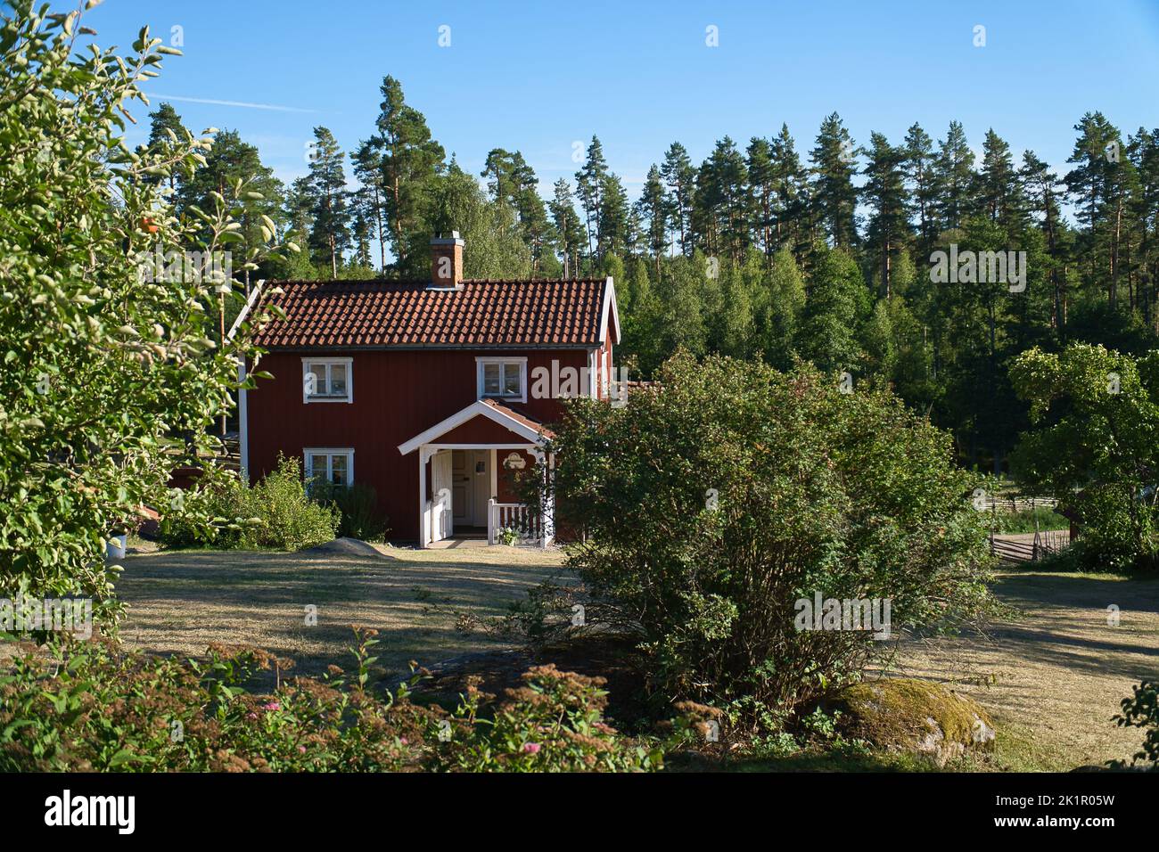 Schwedisches rot-weißes Tratitionhaus in Smalland, Weißer Zaun grüner Garten blauer Himmel. Kindheitserinnerungen aus dem Urlaub in Schweden. Naturfoto Stockfoto