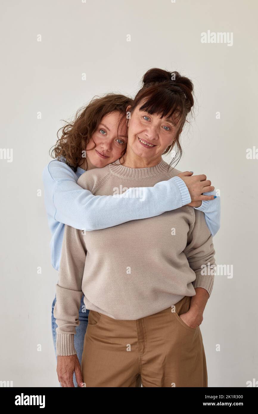 Junge Frau umarmt reife lächelnde Dame in lässiger Kleidung Stockfoto Junge Frau umarmt reife lächelnde Dame in lässiger Kleidung Stockfoto