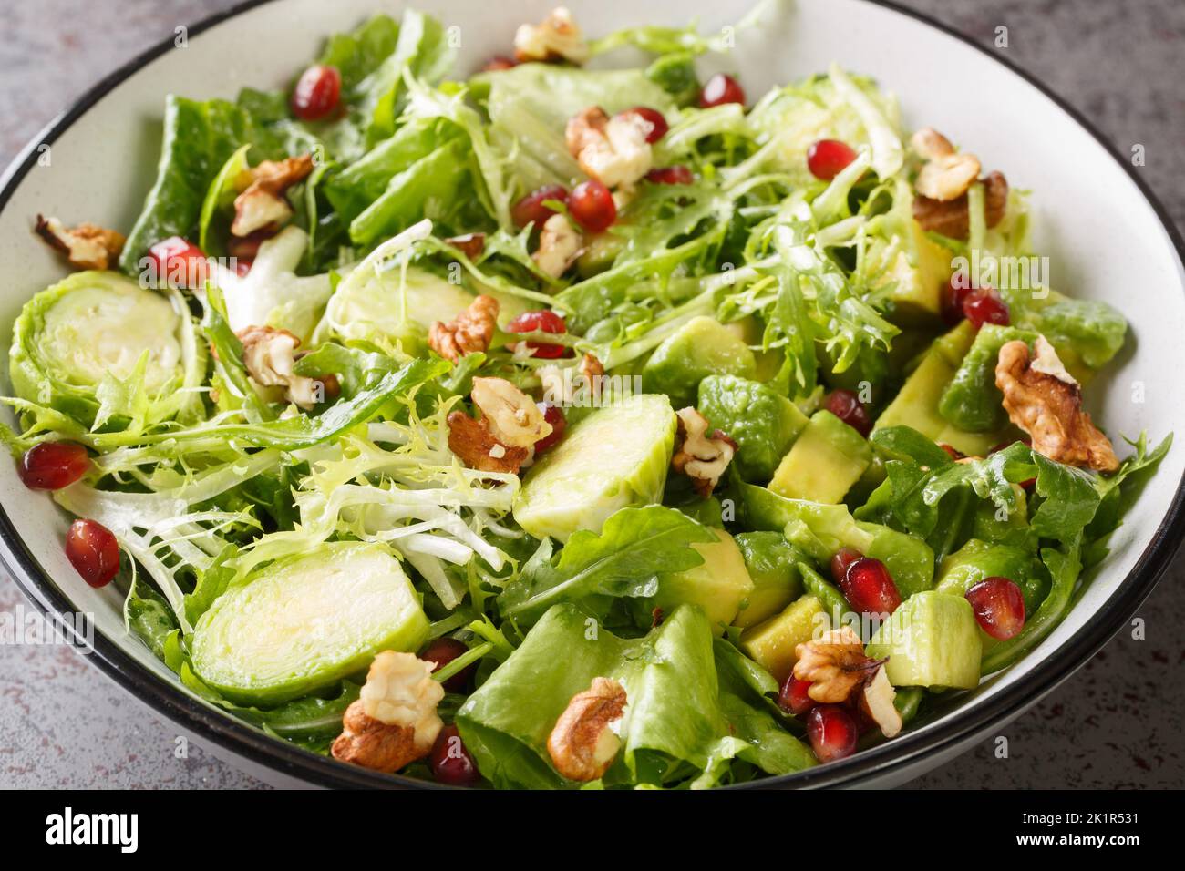 Roher gesunder Salat mit Rosenkohl, Granatapfel, Avocado, Walnüssen und Salat in der Schüssel auf dem Tisch. Horizontal Stockfoto