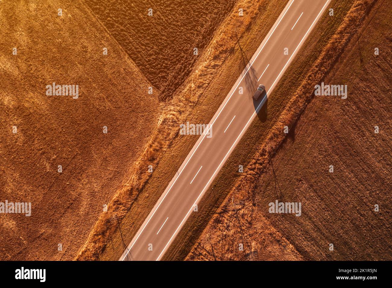 Dunkler PKW, der bei sonnigem Herbstuntergang die Autobahn entlang fährt, Luftaufnahme von Drohne pov, direkt darüber Stockfoto