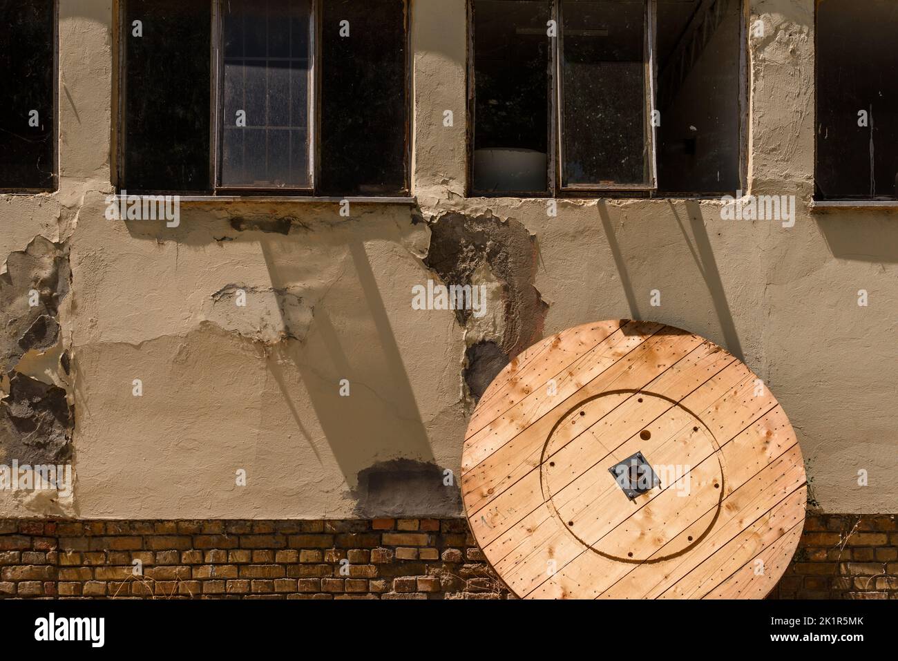 Teil einer hölzernen Kabelrolle, die sich an ein verlassene Industriegebäude in schlechtem Zustand anlehnt, Kopierraum Stockfoto