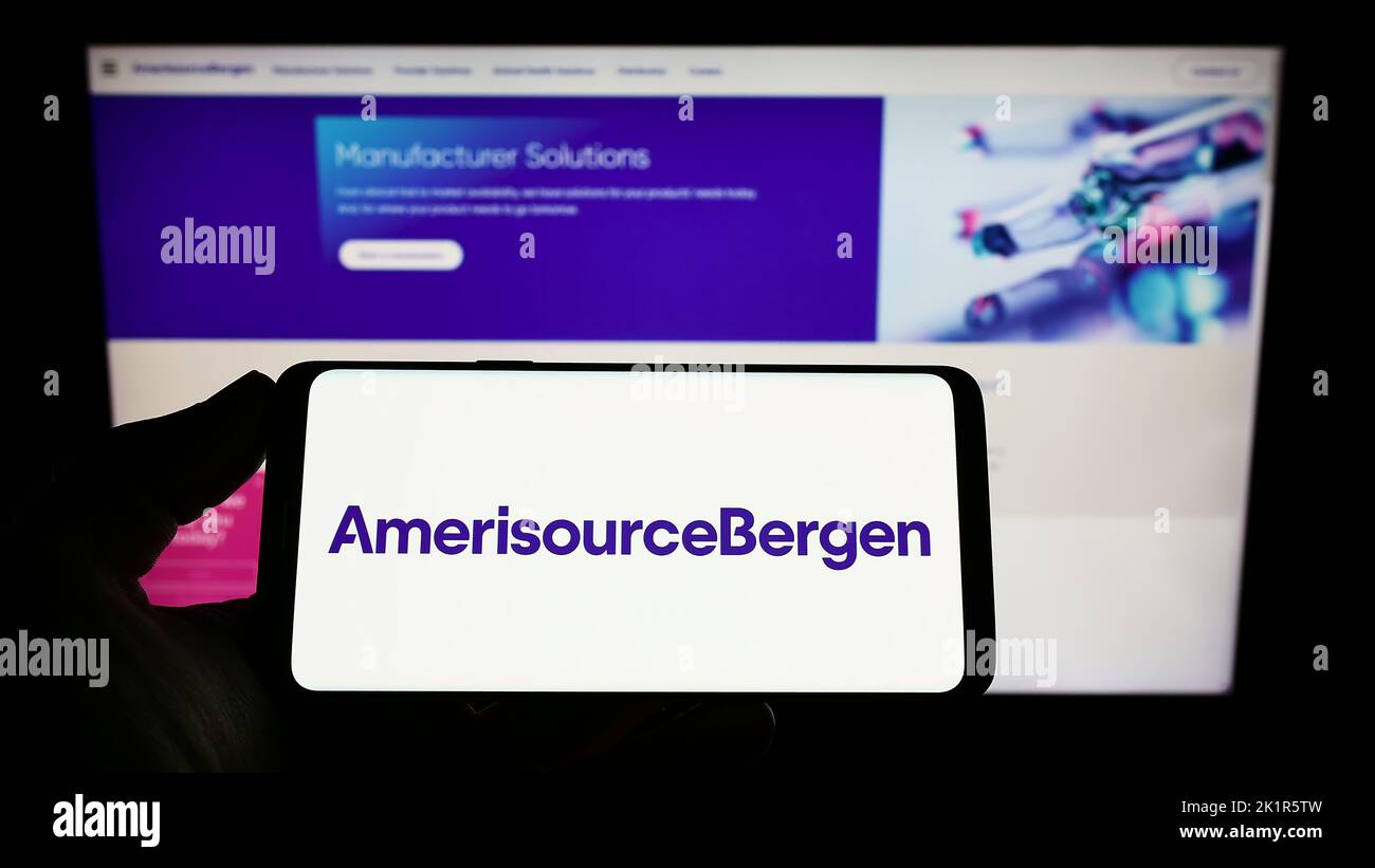 Person, die das Smartphone mit dem Logo des US-amerikanischen Pharmaunternehmens AmerisourceBergen Corporation auf dem Bildschirm vor der Website hält. Konzentrieren Sie sich auf die Telefonanzeige. Stockfoto