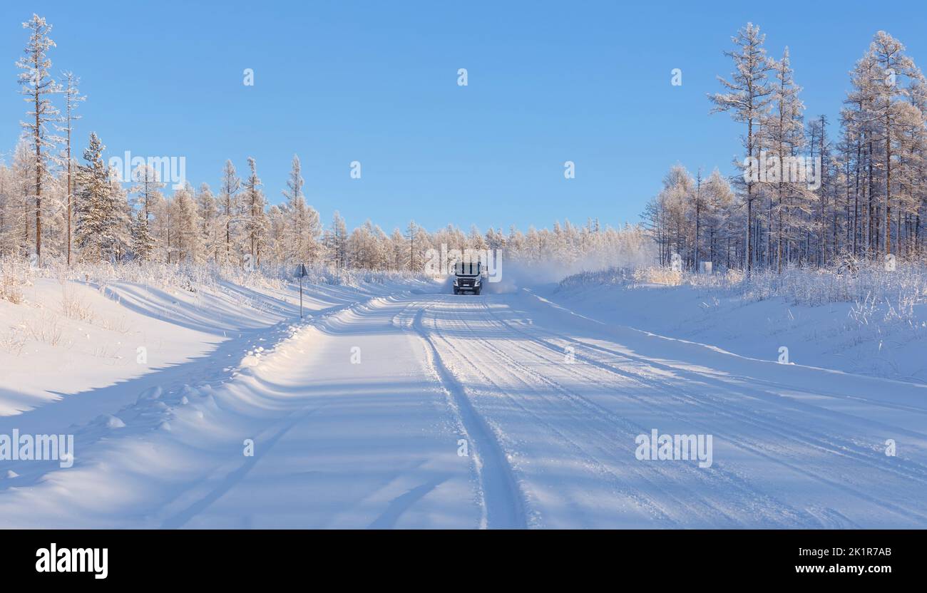 Winterstraße im Wald mit einem fahrenden Auto. Winterliche Straßenlandschaft. Stockfoto