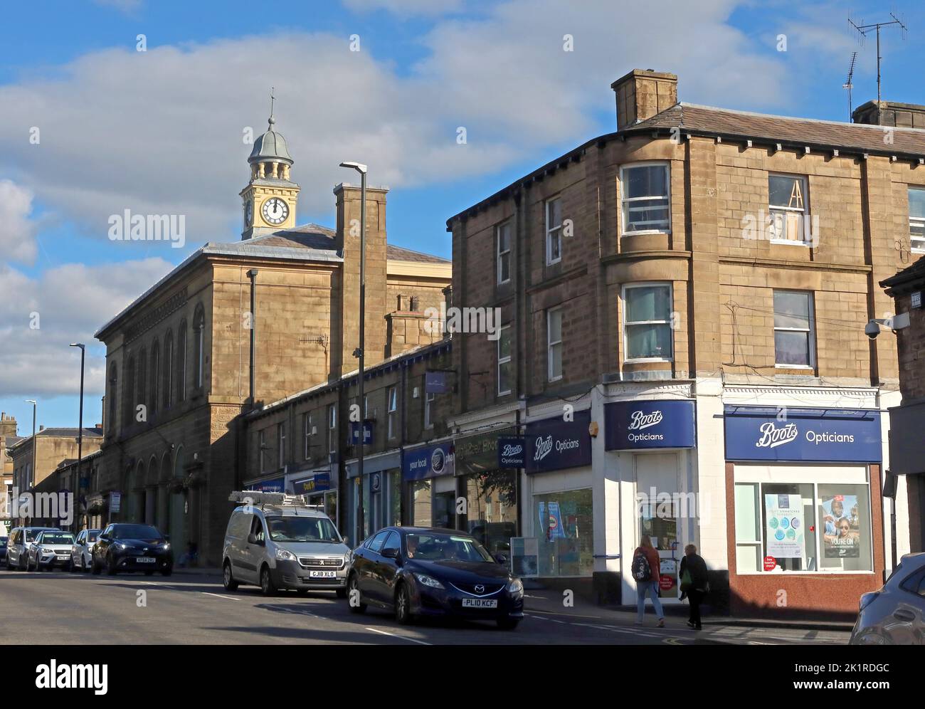 Blick auf das Rathaus von Glossop, den Uhrturm und die Geschäfte der High Street West, darunter Boots Opticians, Glossop, High Peak, Derbyshire, ENGLAND, GROSSBRITANNIEN, SK13 8AL Stockfoto