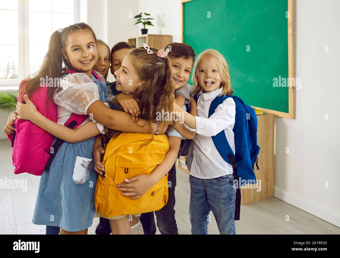 Glückliche kleine Grundschüler umarmen sich nach dem Treffen im Klassenzimmer. Stockfoto