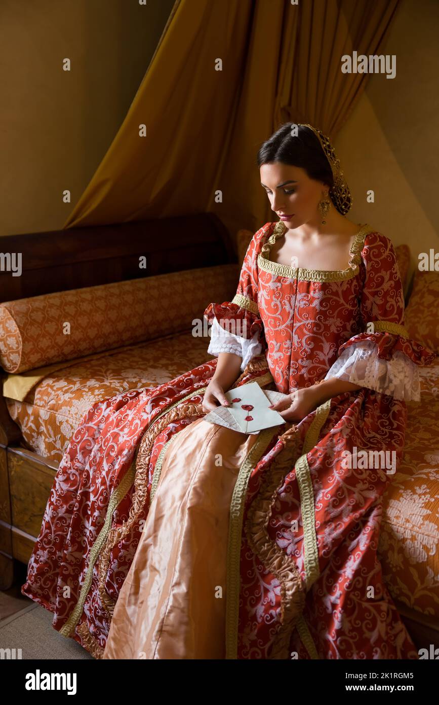 Renaissance-Dame in spätmittelalterlichem Kleid sitzt auf einem schönen Himmelbett in ihrem Schloss Schlafzimmer Stockfoto