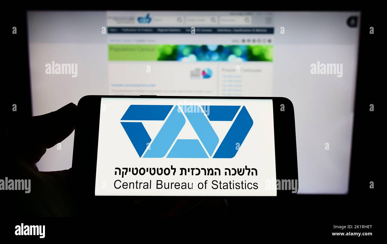 Person mit Mobiltelefon und Logo des israelischen Zentralbüros für Statistik (CBS) auf dem Bildschirm vor der Webseite. Konzentrieren Sie sich auf die Telefonanzeige. Stockfoto