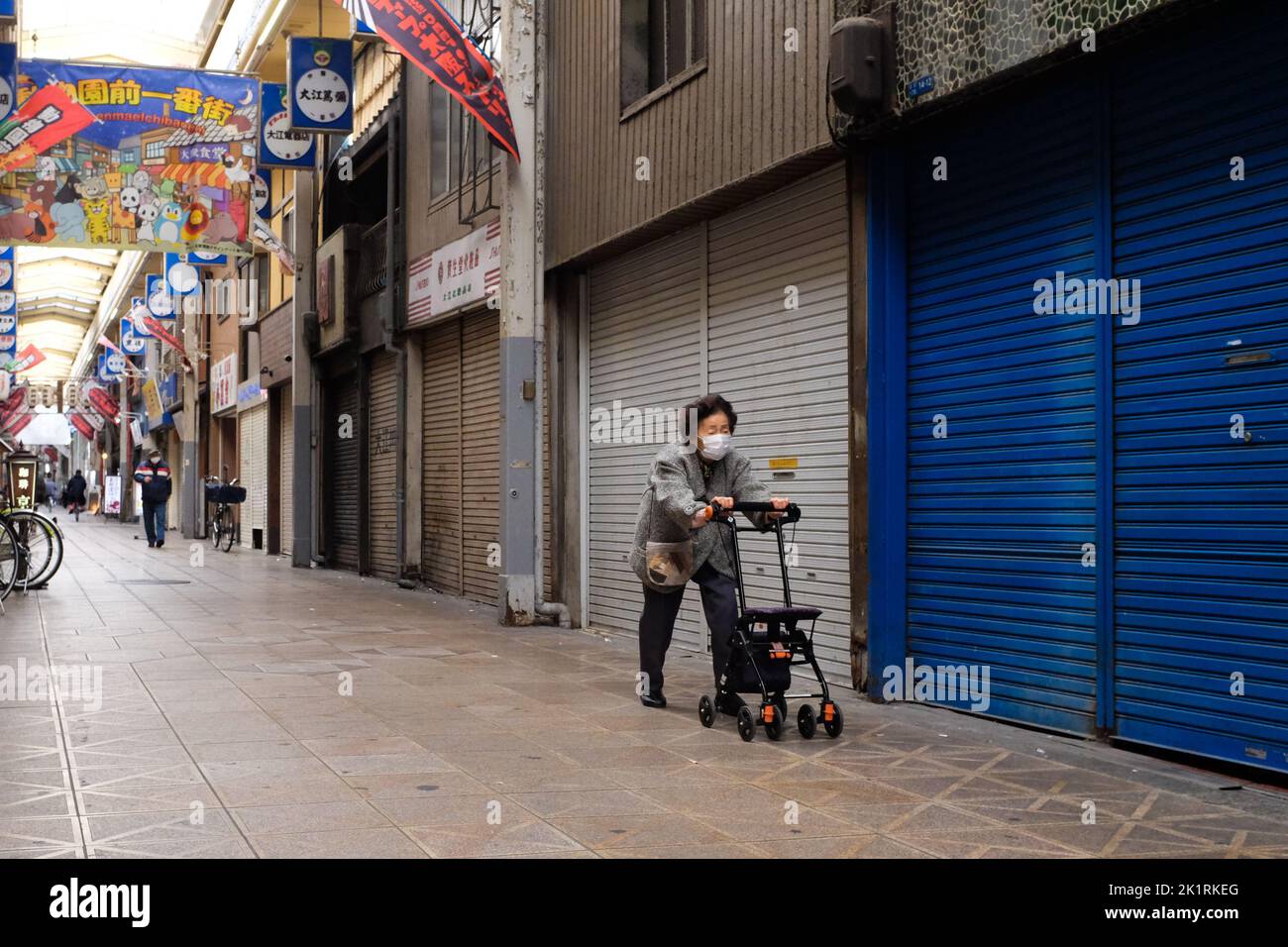 Eine ältere Frau geht entlang einer überdachten Einkaufsstraße in Osaka, Japan. Stockfoto
