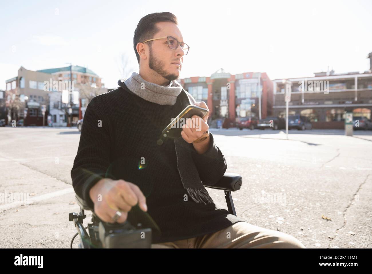 Mann im motorisierten Rollstuhl mit Smartphone auf der sonnigen städtischen Straße Stockfoto