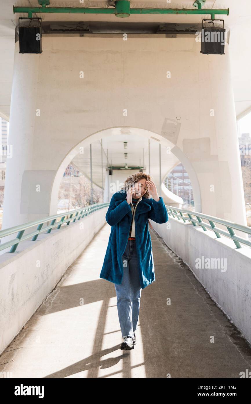 Glückliche Frau, die auf einem Smartphone auf einer Fußgängerbrücke in der Stadt spricht Stockfoto