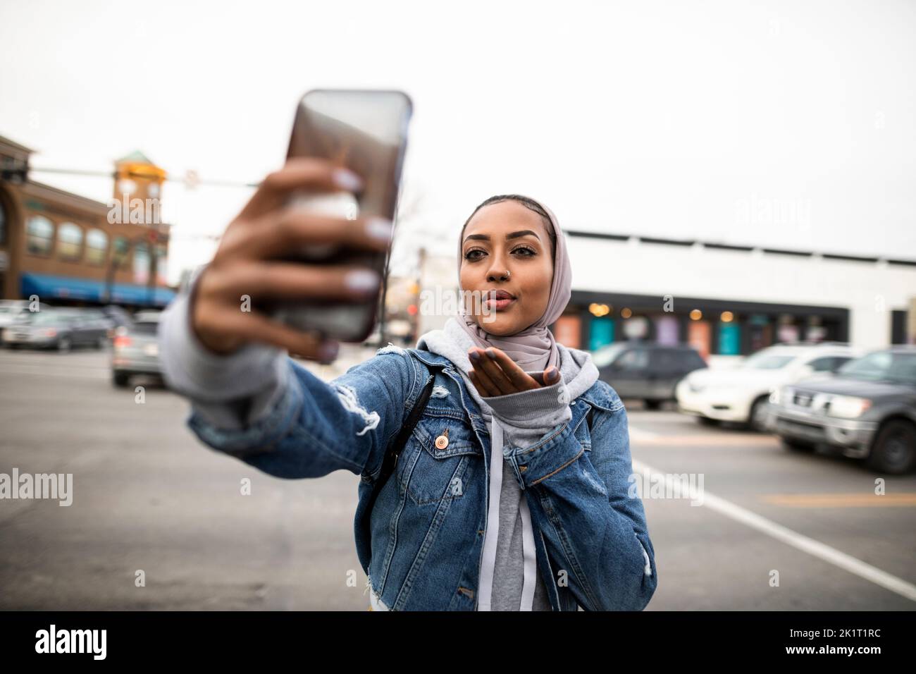 Junge Frau, die ein Selfie mit dem Kameratelefon macht und einen Kuss auf die städtische Straße bläst Stockfoto