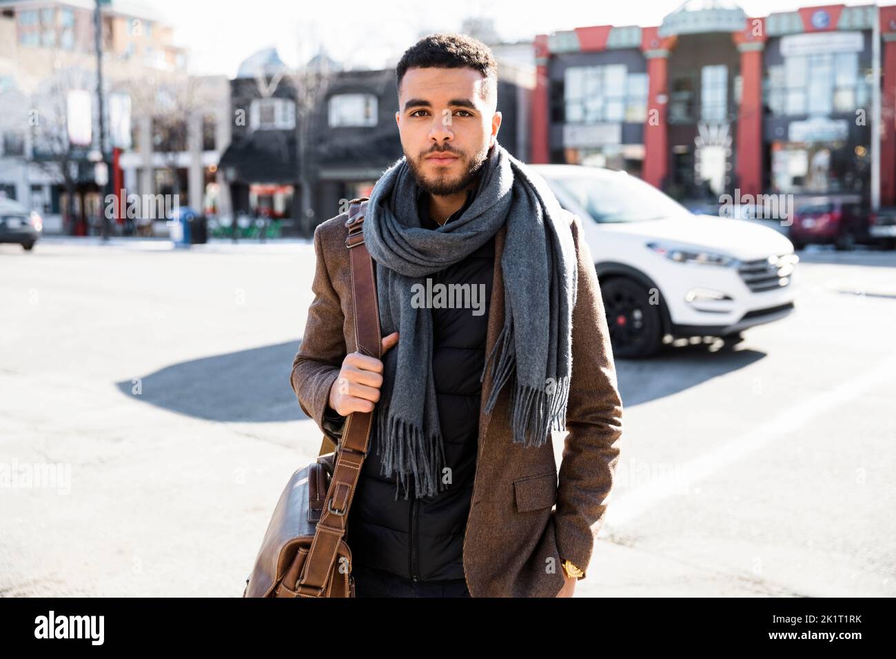 Portrait selbstbewusster junger Geschäftsmann, der die sonnige städtische Straße überquert Stockfoto