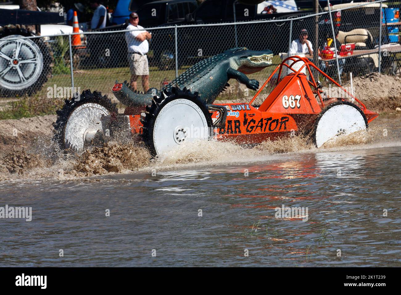 Sumpfbuggy, der sich durch Wasser bewegt, orange, Aktion, große Alligatorfigur oben, Zuschauer, Wasserspray, Schlammspritzer, Bewegung, Jeep-Stil, Fahrzeug s Stockfoto