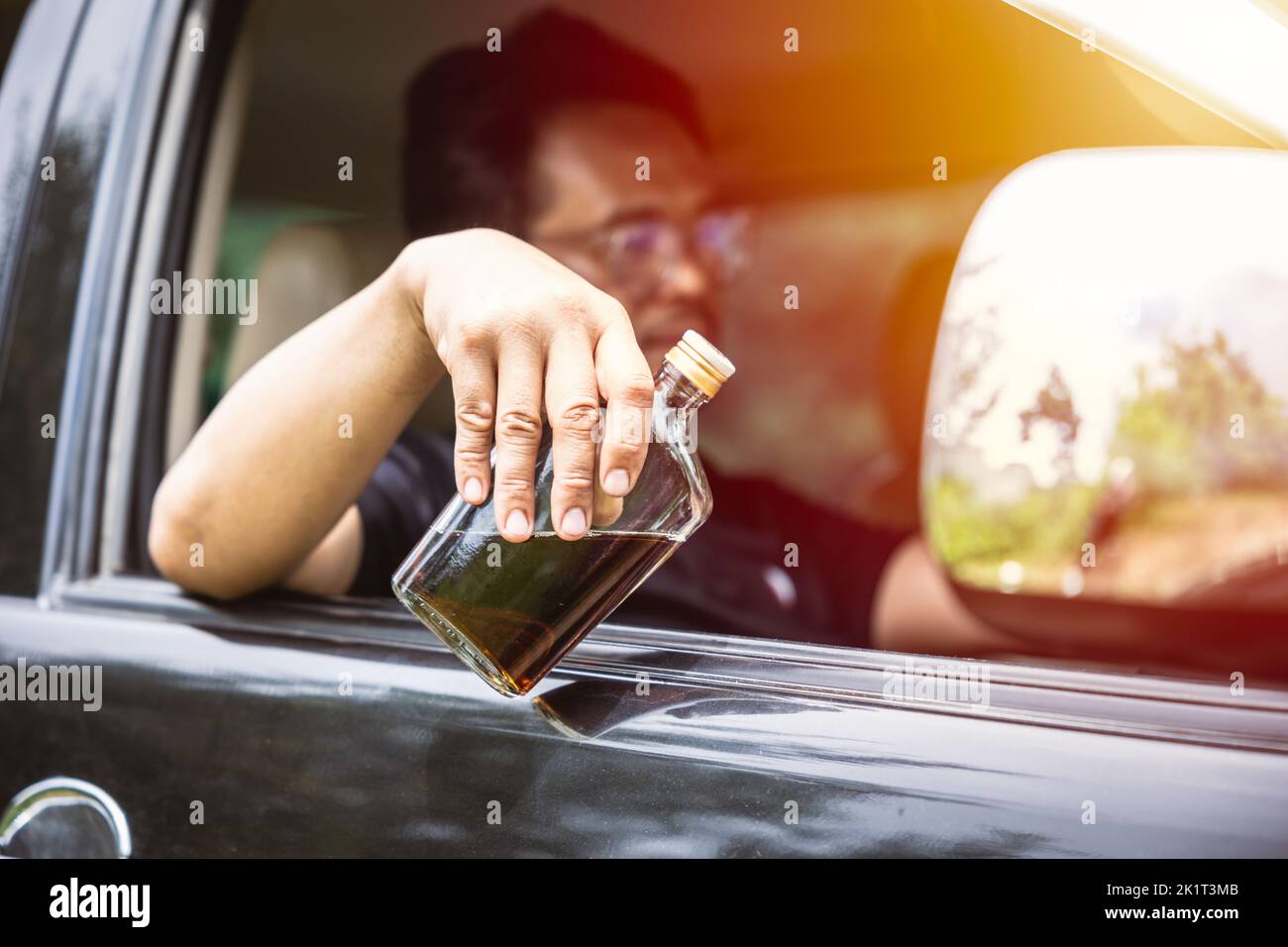 Mann betrunken während der Fahrt ein Auto. Fahrer mit Alkohol Whisky Flasche gefährlich und illegal Konzept. Stockfoto