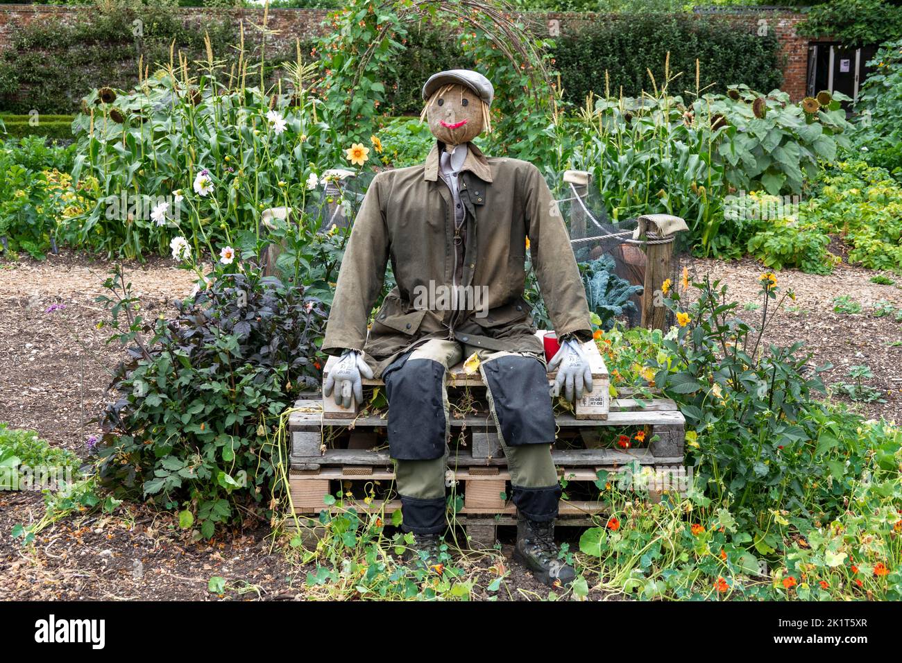 Gärtner Vogelscheuche sitzt auf Kisten im Garten zwischen Blumen und Pflanzen Stockfoto