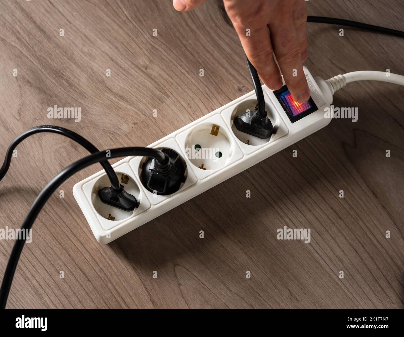 Ein Mann, der den elektrischen Strom abschaltet, indem er die Taste an einer weißen Steckdose abschaltet, um den Energieverbrauch zu senken Stockfoto