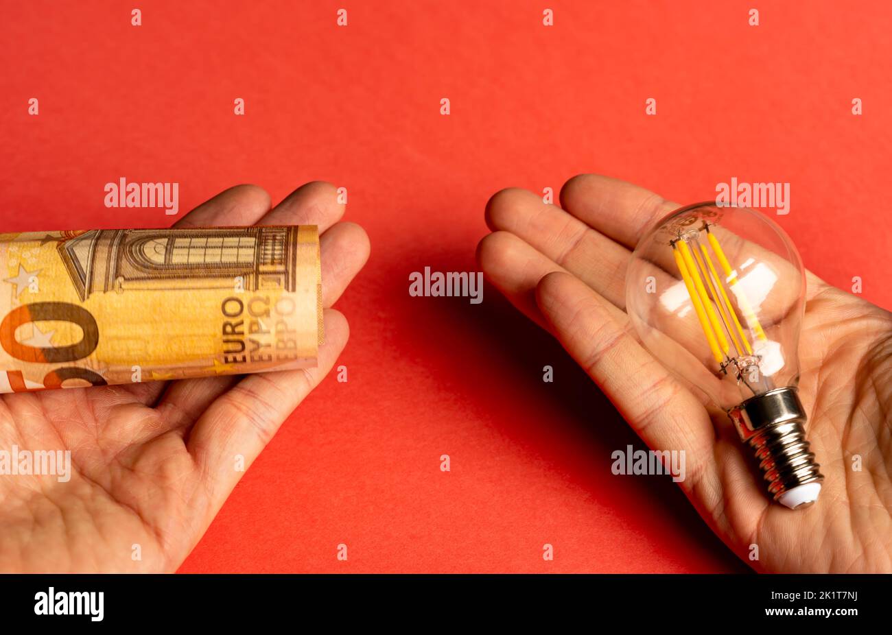 Mann, der in jeder Hand eine Glühbirne und eine Euro-Banknote hält. Konzept der Entscheidung zwischen Geld oder Energie. Stockfoto
